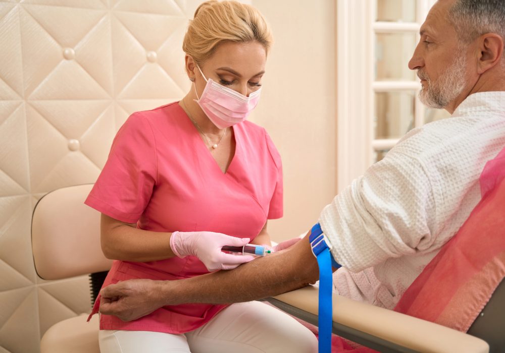 Pretty female nurse taking a blood test from vein Pretty female nurse taking blood test from vein while the patient looks at her in medical clinic